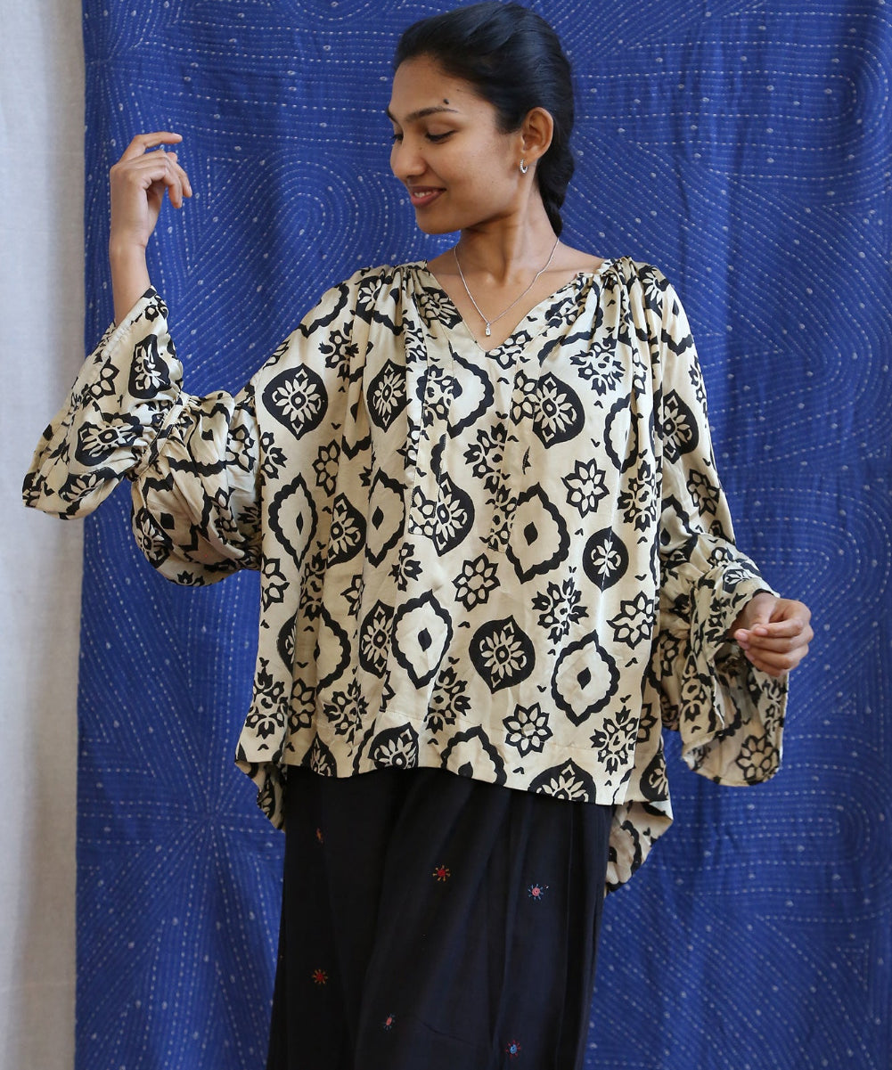 Woman wearing a patterned blouse against a blue curtain