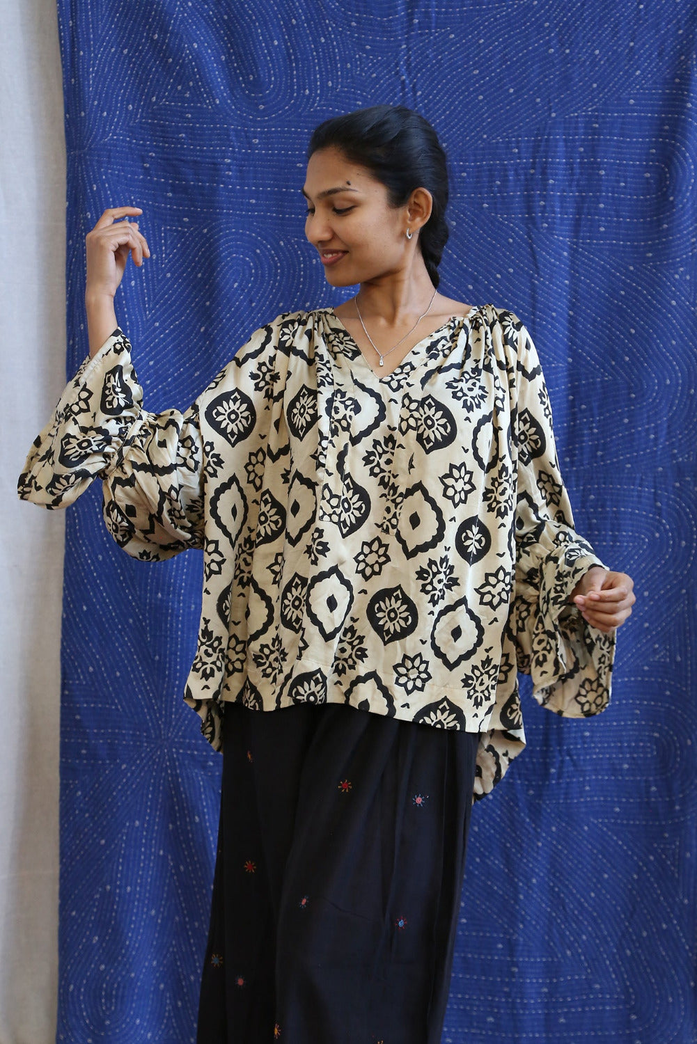 Woman wearing a patterned blouse against a blue curtain