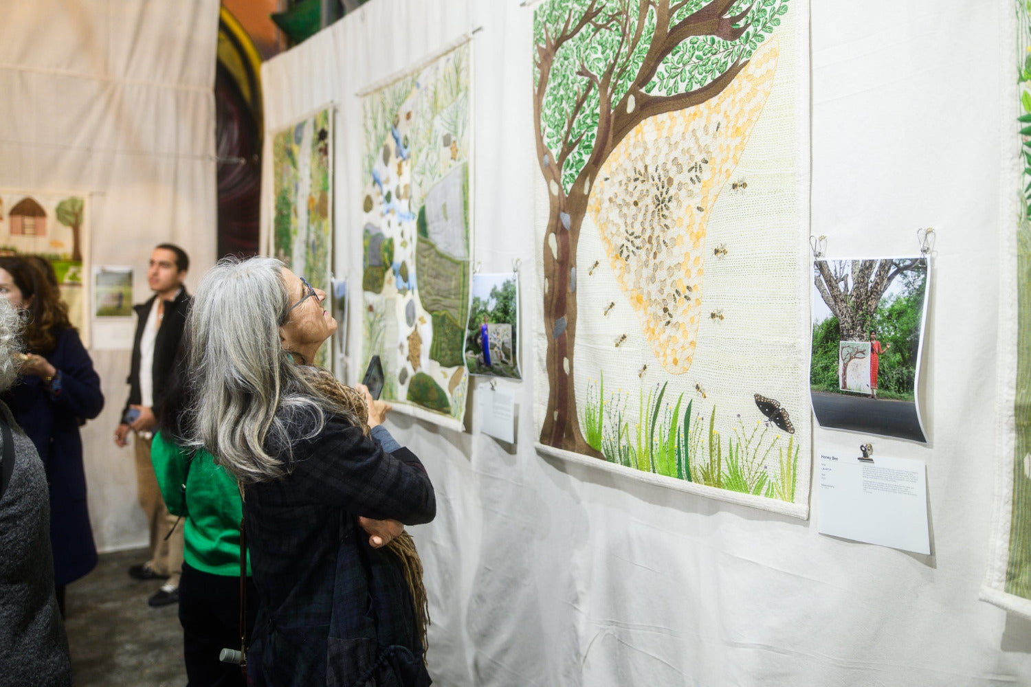 Art exhibition with people looking at artwork on a wall.