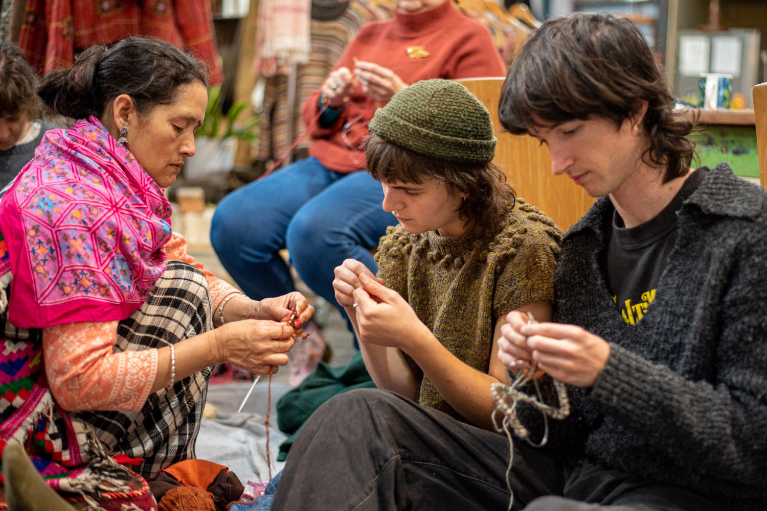 Three people engaged in knitting activities in a cozy indoor setting.