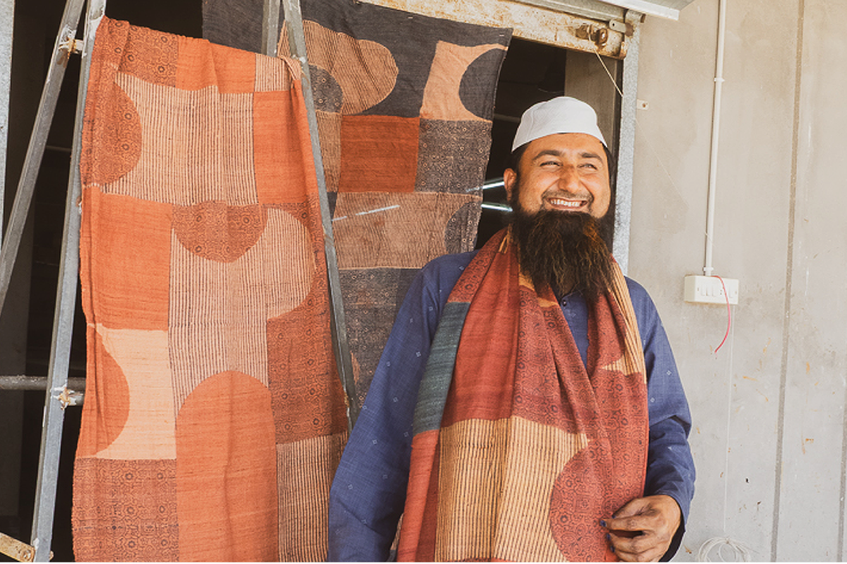 Man holding a block-printed fabric with text about Sufiyan Khatri, a master ajrakh blockprinter.