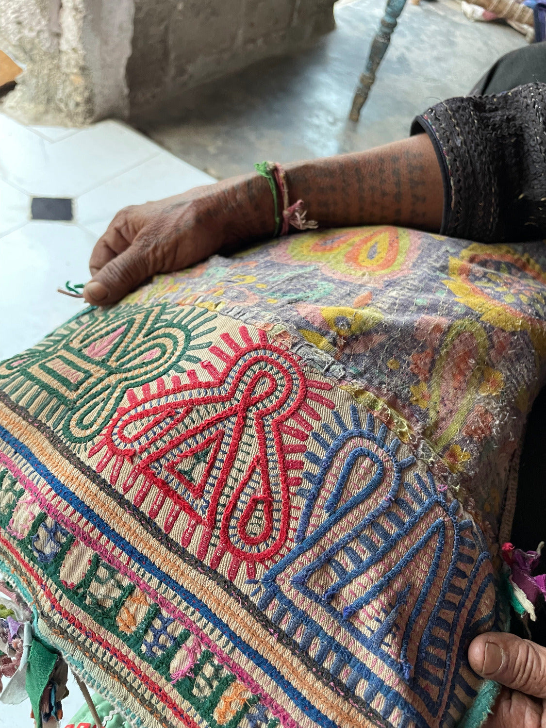 Colorful embroidered fabric held by a person with tattoos on their arm.