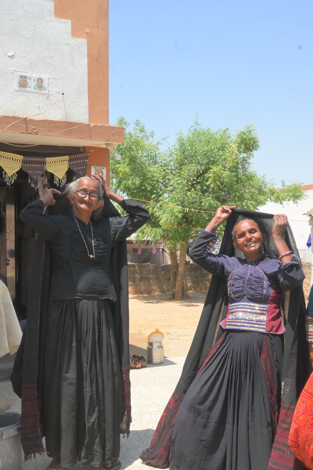 Two women in traditional black attire with a child in a blue dress, standing outdoors.