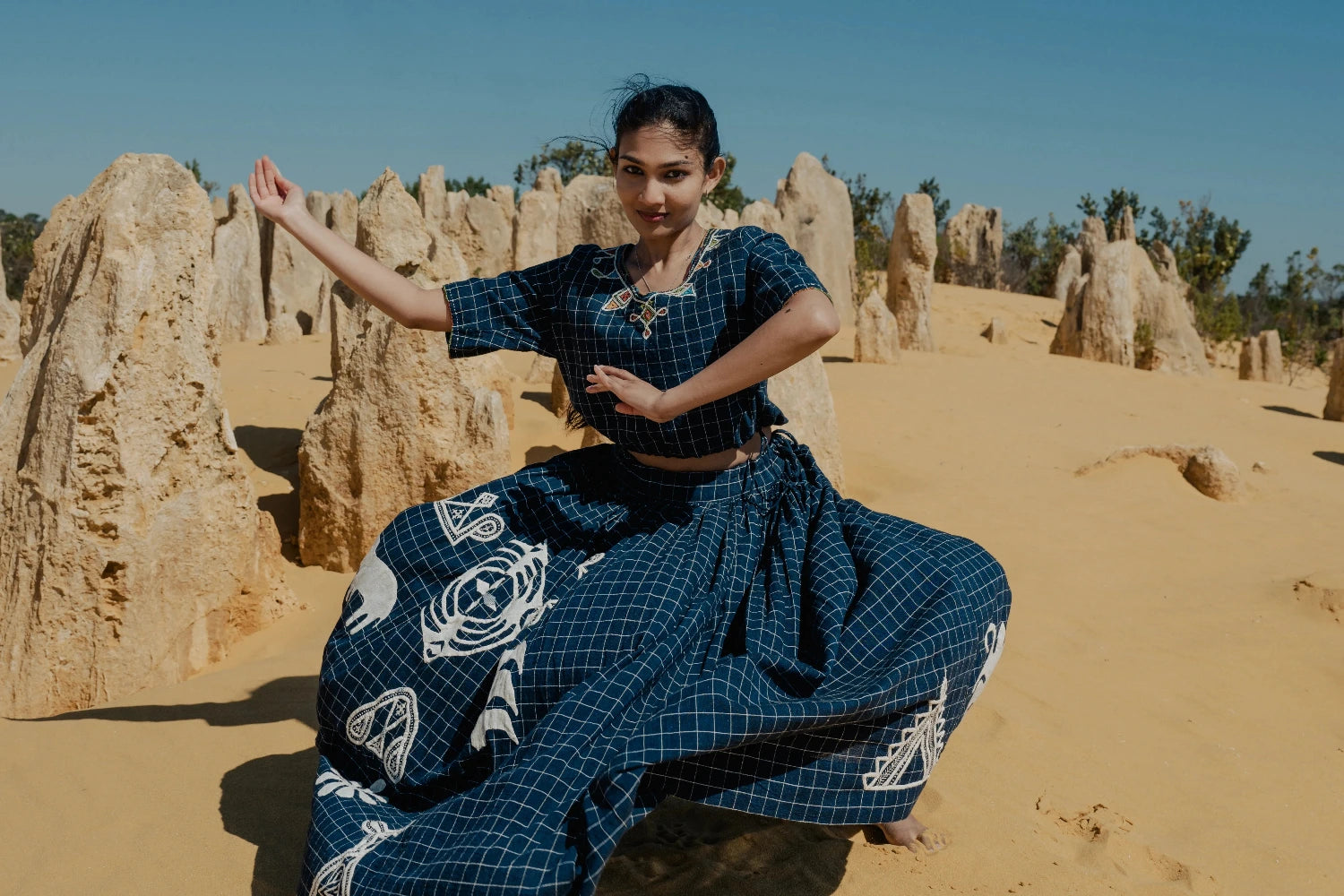Woman in traditional blue outfit posing in a desert landscape with rock formations.