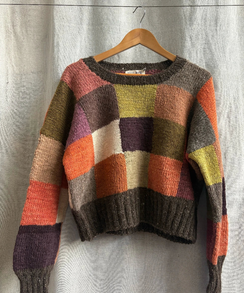 Multicolored sweater on a wooden hanger against a neutral background