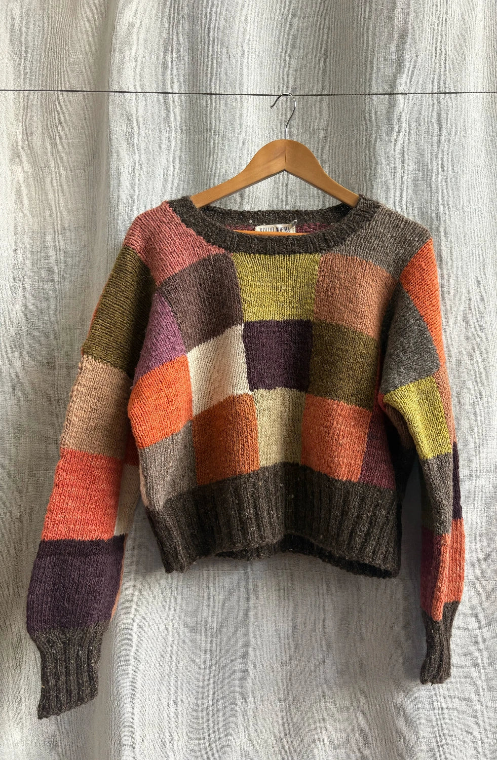 Multicolored sweater on a wooden hanger against a neutral background
