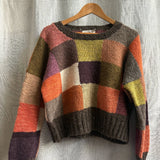 Multicolored sweater on a wooden hanger against a neutral background